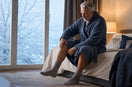 Adult gently moving a stiff knee beside a window on a cold winter morning